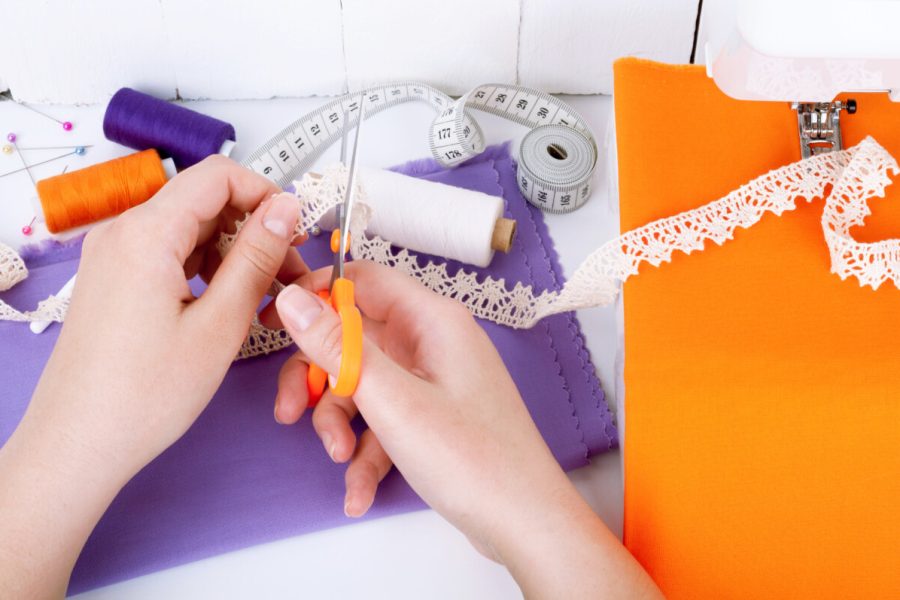 Sewing and making clothes on the sewing machine. Cotton fabric, lace, spool of thread, scissors, measuring tape on white wooden background. Set of sewing accessories for needlework. Sewing background concept